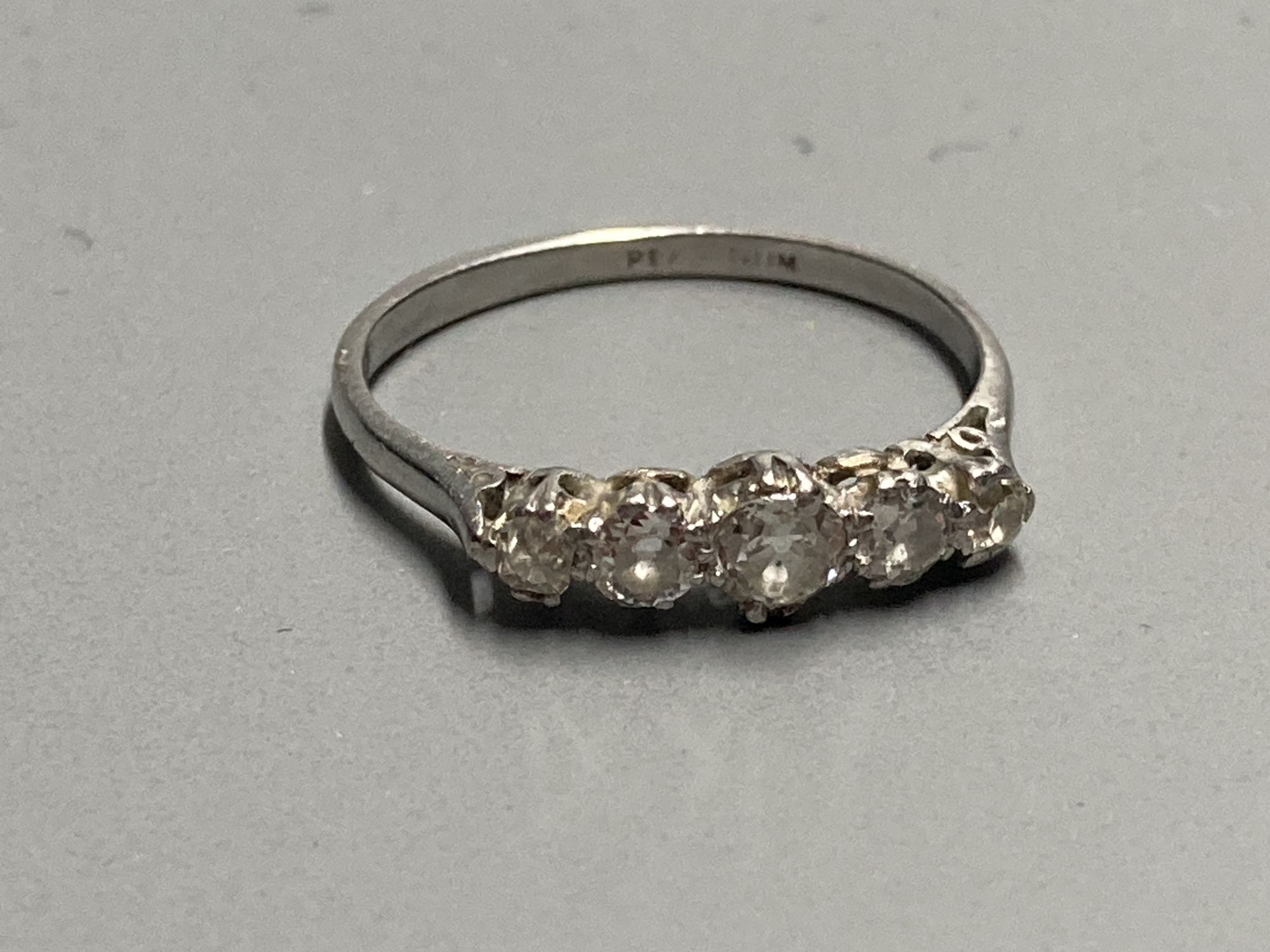 A 1940s/1950s white metal (stamped platinum) and graduated five stone diamond set half hoop ring, size K/L, gross 2.4 grams.